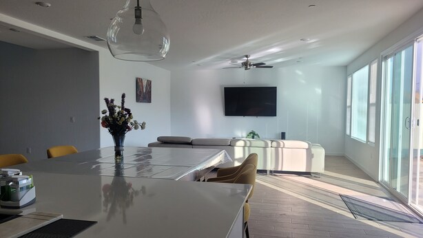 A modern living room with a large island table, a sofa, and a TV. - Sequoia Deluxe / Brand New 5 beds/ 3.5 baths  (Visalia)