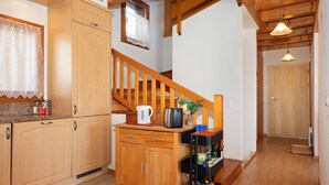A kitchen with wooden cabinets, a coffee maker, a kettle, and a cart with bottles. - Orchidée by Interhome (Ovronnaz)