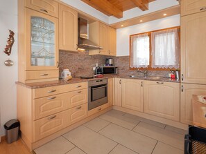 A kitchen with wooden cabinets, a granite countertop, stainless steel appliances, and a window with curtains. - Orchidée by Interhome (Ovronnaz)