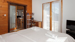A hotel room with a wooden interior, a bed with white linens, a desk with a chair, a television, and a sliding glass door leading to a balcony. - Orchidée by Interhome (Ovronnaz)