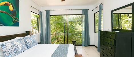 A bedroom with a bed, a ceiling fan, a dresser, and a large window with curtains.