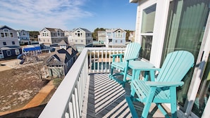 A balcony with a view of neighboring houses, a wooden deck, and two turquoise Adirondack chairs. - Oceanside, Hot Tub, Community Pool, CB51, OBXcape (Corolla)