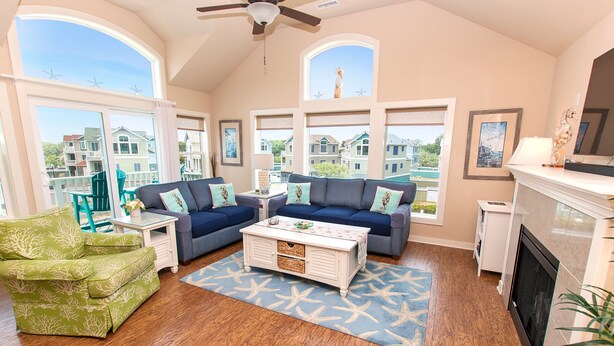 A living room with a blue sofa, a green armchair, a white coffee table, and a fireplace. - Oceanside, Hot Tub, Community Pool, CB51, OBXcape (Corolla)