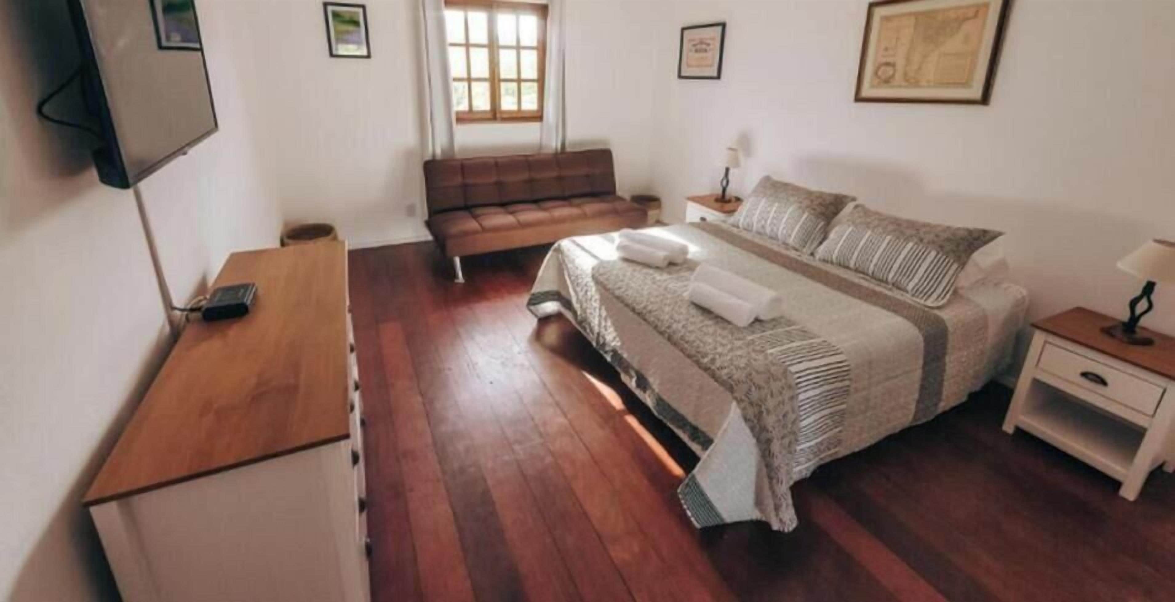 A bedroom with a bed, a wooden desk, a sofa, a nightstand, and a TV.