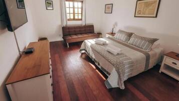 A bedroom with a bed, a wooden desk, a sofa, a nightstand, and a TV.
