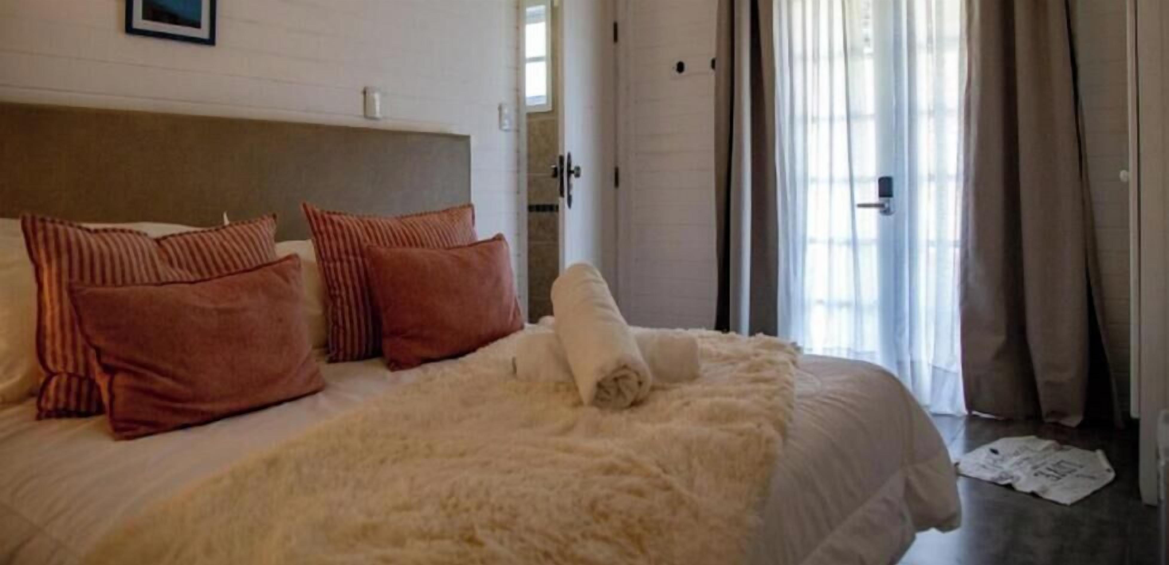 Una cama bien hecha con almohadas, un edredón blanco mullido y una toalla enrollada.
