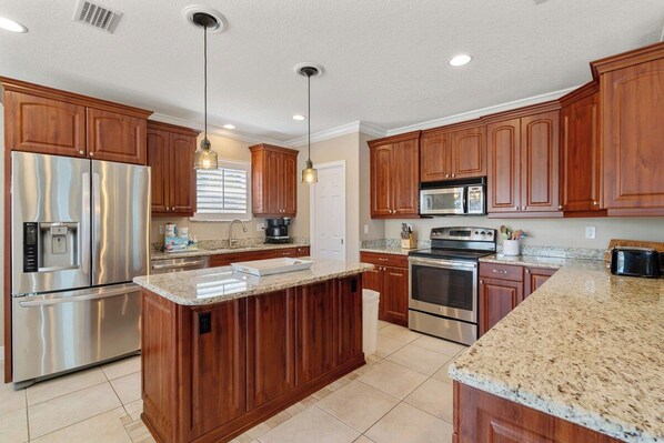 A modern kitchen with wooden cabinets, stainless steel appliances, granite countertops, and pendant lighting.
