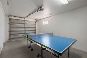 A ping pong table in a room with a garage door and a small window.