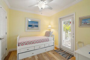 A bedroom with a bed, a ceiling fan, a door with blinds, a framed picture on the wall, and a small table.