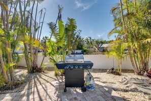 Un barbecue à gaz, avec une bouteille de propane, entouré de palmiers et donnant sur une terrasse dallée.