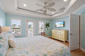 Ein Schlafzimmer mit einem großen Bett, einem Deckenventilator, einem an der Wand befestigten Fernseher und einem Fenster mit Jalousien.
