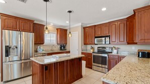 Une cuisine moderne avec des meubles en bois, des appareils en acier inoxydable, des plans de travail en granit et des luminaires suspendus.