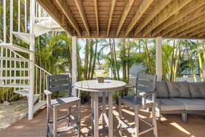 A covered outdoor seating area with a wooden ceiling, white lattice structure, and a view of palm trees.