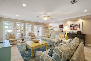 A well-lit living room with a ceiling fan, a sofa set, a coffee table, and a television.
