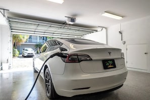 Un Tesla blanco cargando en un garaje con una cámara en el techo.