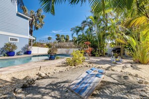 A backyard with a swimming pool, palm trees, and a wooden deck.