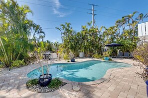 A swimming pool with a curved edge, surrounded by a paved patio and various tropical plants.
