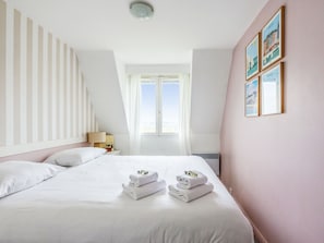 A hotel room with a large bed, a nightstand, a lamp, and a window with a view of the sky.