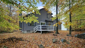 A house with a covered outdoor area, surrounded by trees with autumn leaves. - Peaceful Retreat - Game Room, Central AC & Pet-friendly (Tobyhanna)
