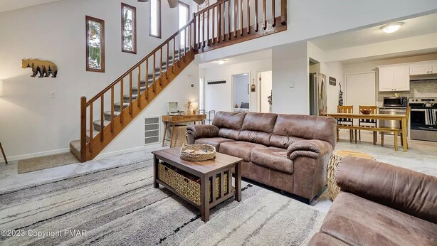 A spacious living area with a leather sofa, a wooden coffee table, and a staircase leading to an upper level. - Peaceful Retreat - Game Room, Central AC & Pet-friendly (Tobyhanna)
