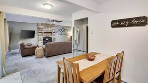 A modern living room with a fireplace, a dining area with a wooden table and chairs, and a kitchen with a refrigerator and stove. - Peaceful Retreat - Game Room, Central AC & Pet-friendly (Tobyhanna)