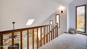 A staircase with a wooden railing, a skylight, and a view of autumn foliage through a window. - Peaceful Retreat - Game Room, Central AC & Pet-friendly (Tobyhanna)