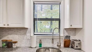A kitchen with white cabinets, a granite countertop, a stainless steel sink, a window with blinds, and a toaster. - Peaceful Retreat - Game Room, Central AC & Pet-friendly (Tobyhanna)