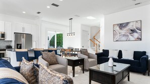 Una sala moderna con un sofá, sillones, una mesa de centro y una zona de comedor con sillas y una mesa.