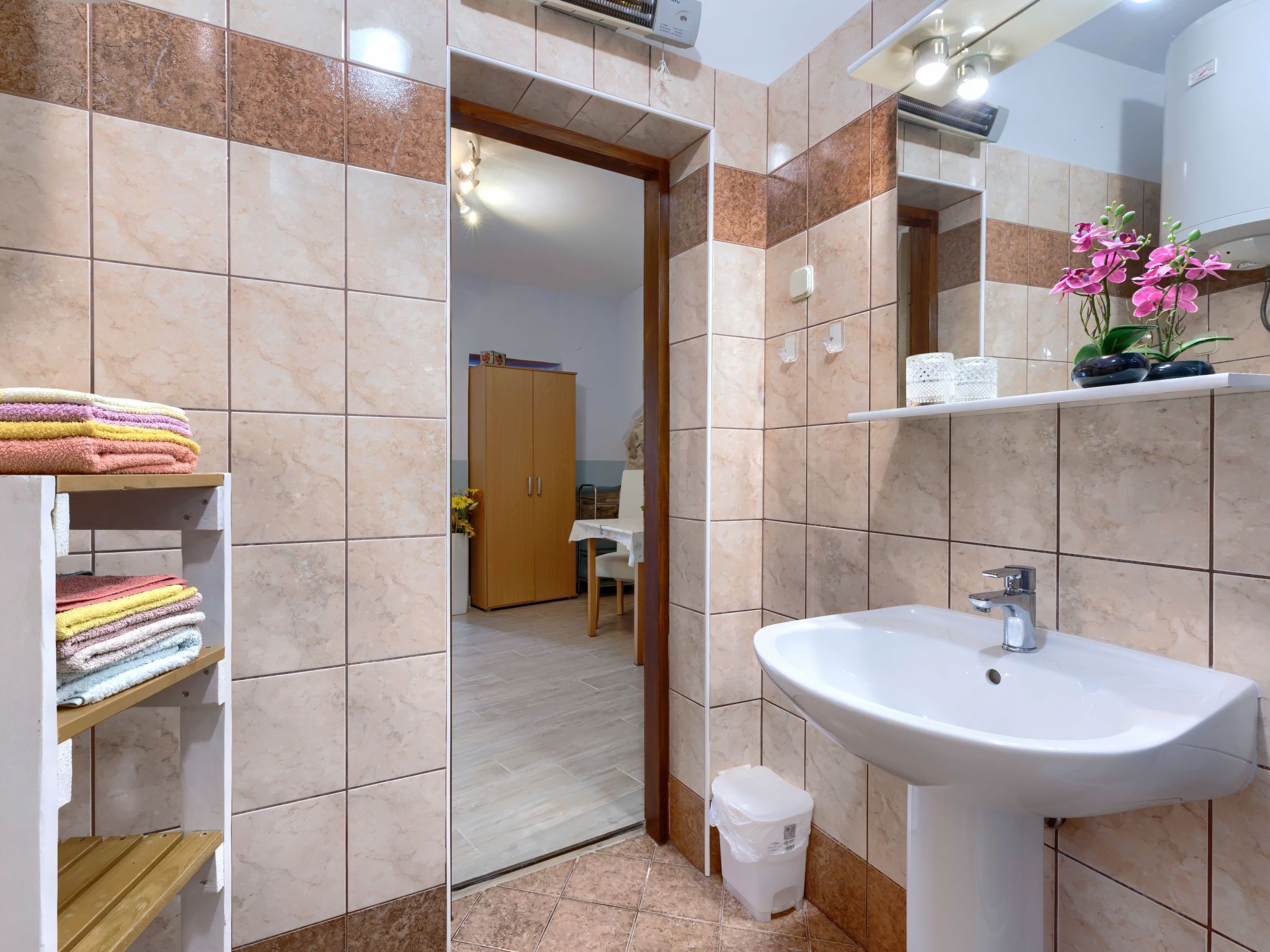 Een badkamer met een wastafel, toilet en spiegel. Handdoeken liggen opgestapeld op planken en er is een kast.