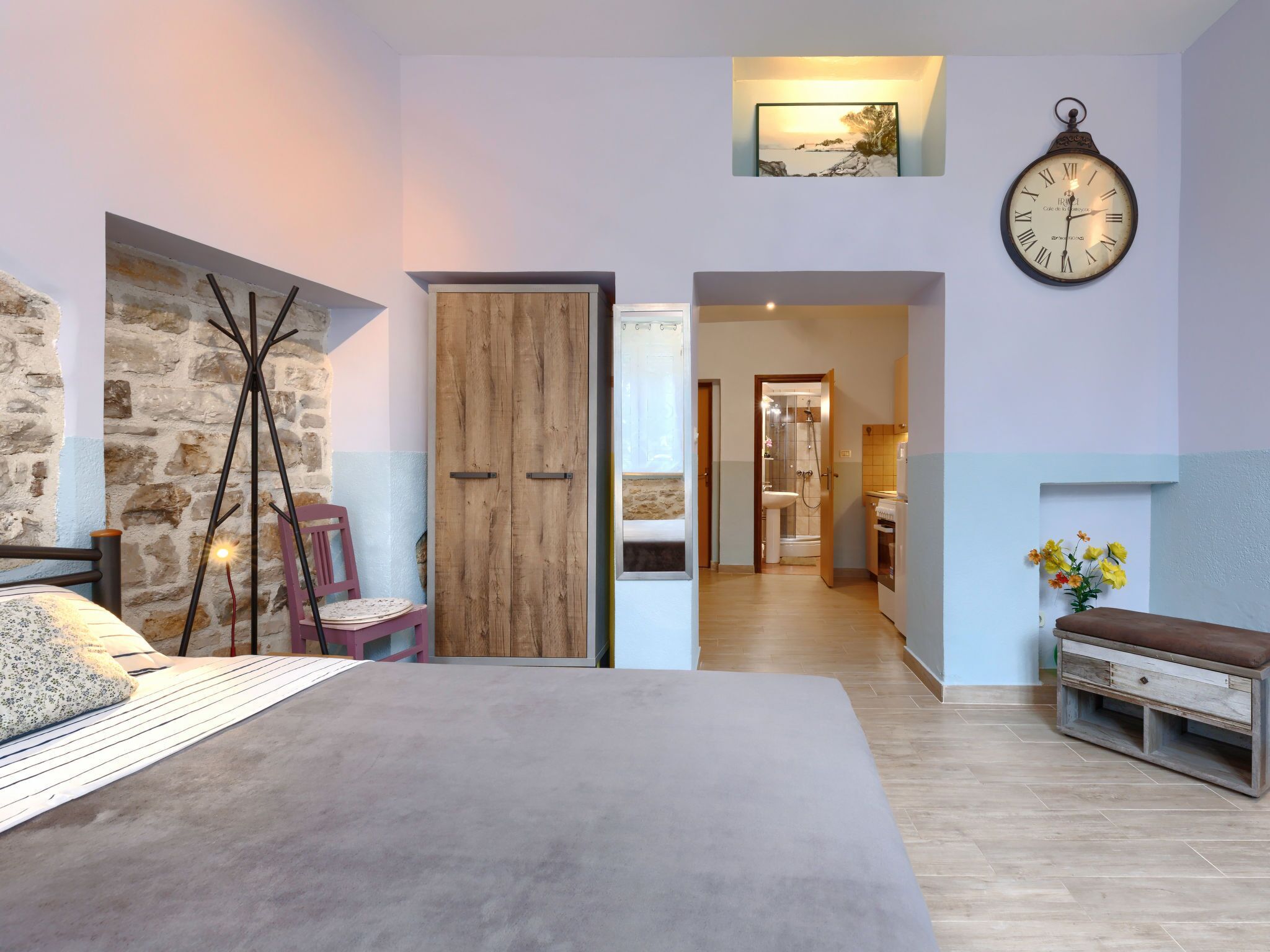 Een slaapkamer met een bed, een houten garderobe, een klok en een badkamer die door een open deur zichtbaar is.