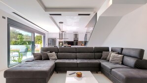 Ein modernes Wohnzimmer mit einer Eckcouch, einem Couchtisch sowie Blick auf die Küche und den Außenbereich.