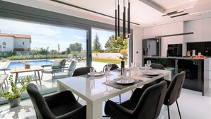 Ein moderner Essbereich mit einem Glastisch, schwarzen Stühlen und Blick auf Pool und Garten.