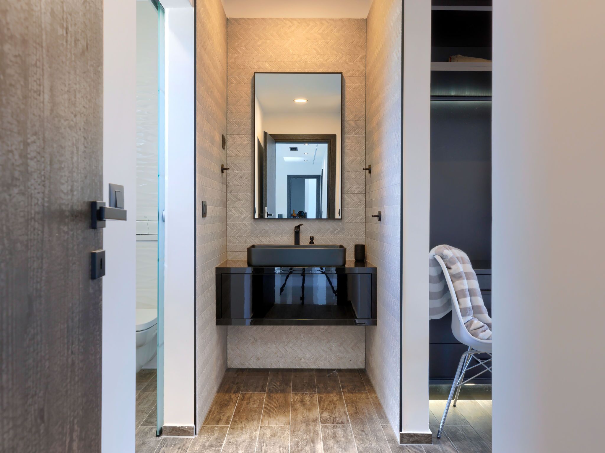 Une salle de bain moderne avec un grand miroir, un lavabo foncé et une chaise.