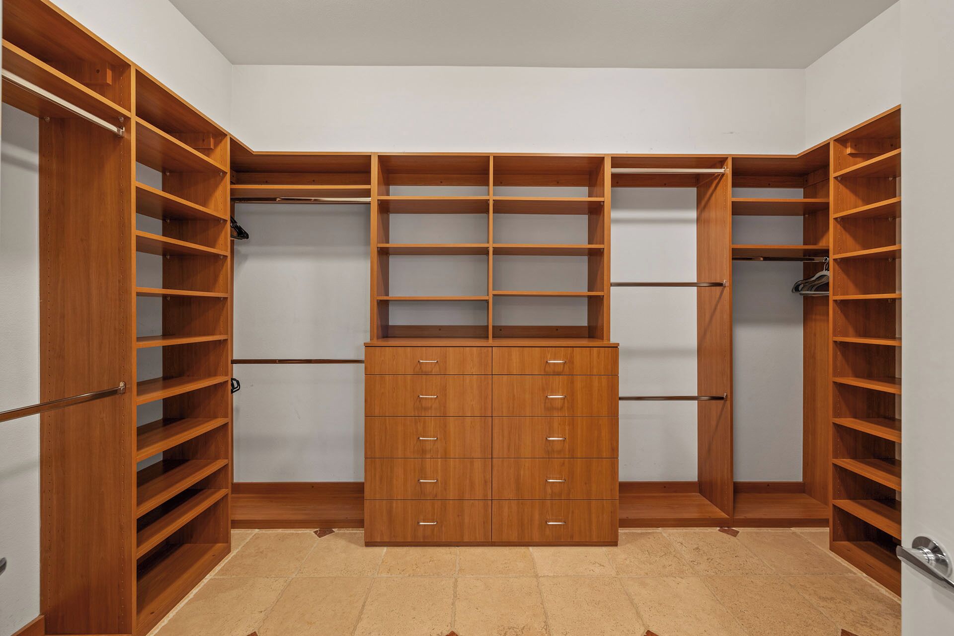 Un dressing avec de nombreuses étagères et tiroirs en bois, un meuble de rangement central et une tringle pour suspendre les vêtements.
