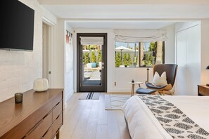 Un dormitorio moderno con cama, una silla, un escritorio y una ventana con vistas a zonas verdes.