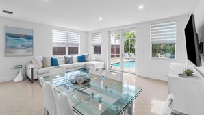A modern living room with a glass dining table, white sofas, and large windows with blinds. - BY THE SEA VACATION VILLAS 4 BED/PRIVATE POOL/STEPS TO THE BEACH (Lauderdale-by-the-Sea)