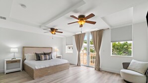 A bedroom with a bed, two nightstands, a ceiling fan, a window with curtains, and a view of greenery outside. - BY THE SEA VACATION VILLAS 4 BED/PRIVATE POOL/STEPS TO THE BEACH (Lauderdale-by-the-Sea)