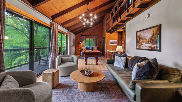 Ein geräumiges Wohnzimmer mit Holzboden, einem Billardtisch und einem großen Fenster mit Blick auf einen Wald.