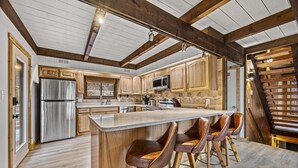 Eine moderne Küche mit Holzausbau, einem Edelstahl-Kühlschrank, einer Mikrowelle und einer großen Kücheninsel mit Barhocker.