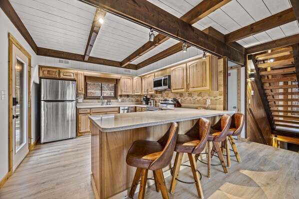 A modern kitchen with wooden cabinets, a stainless steel refrigerator, a microwave, and a large island with bar stools.