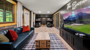 Ein modernes Zimmer mit einem schwarzen Ledersofa, einem Holztisch und einem großen Fernseher, der eine schöne Landschaft zeigt.