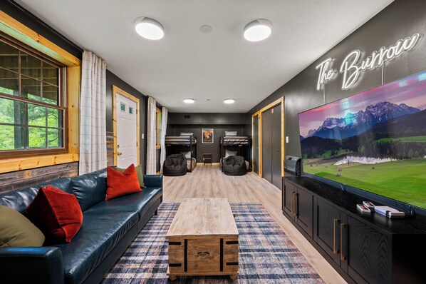 A modern room with a black leather sofa, a wooden coffee table, and a large TV screen displaying a scenic landscape.
