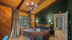Ein Schlafzimmer mit Holzwänden, einem Bett, einem Nachttisch, einer Wandlampe und Blick ins Freie.