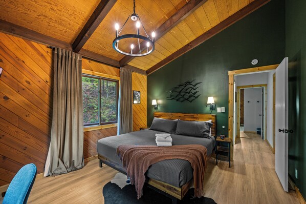 Un dormitorio con paneles de madera, una cama, una mesita de noche, una lámpara de pared y vistas al exterior.