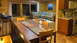 A cozy living room with a wooden floor, a dining table with chairs, a sofa, and a kitchen area with a stove and cabinets. - Lake Lucerne Family Getaway, private setting close to town (Crandon)