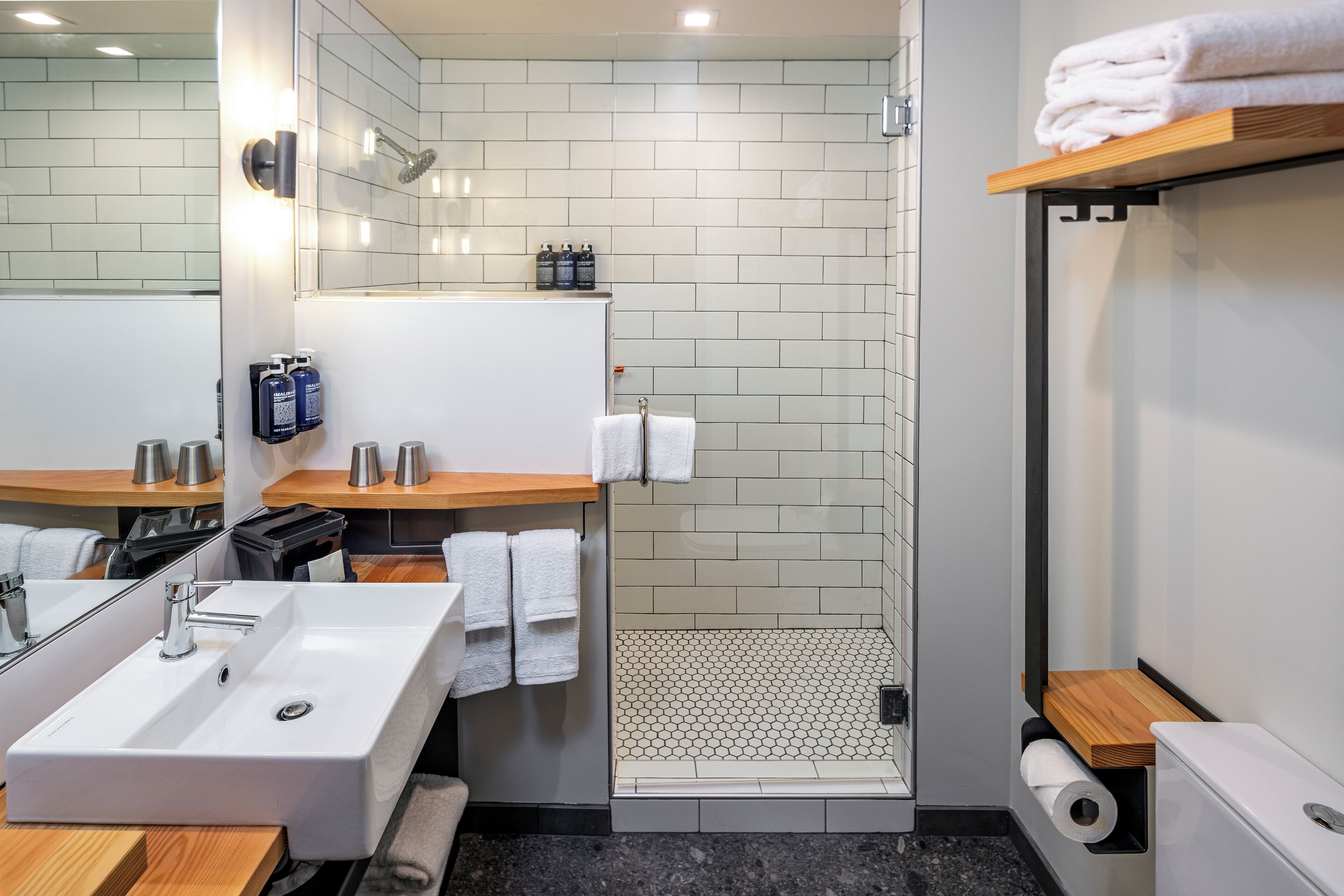 Un baño moderno con lavamanos, espejo y ducha blancos. Hay toallas y artículos de aseo en la encimera.