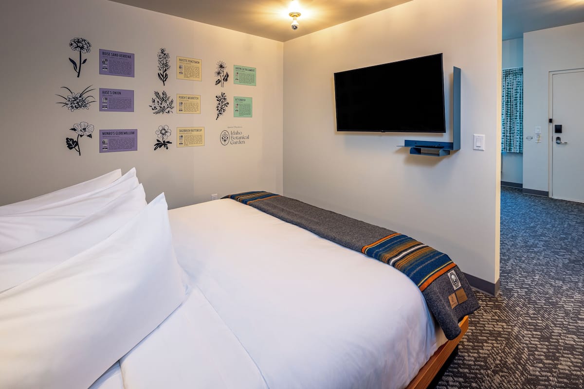 Quarto de hotel com cama, televisão de tela plana na parede e arte botânica.