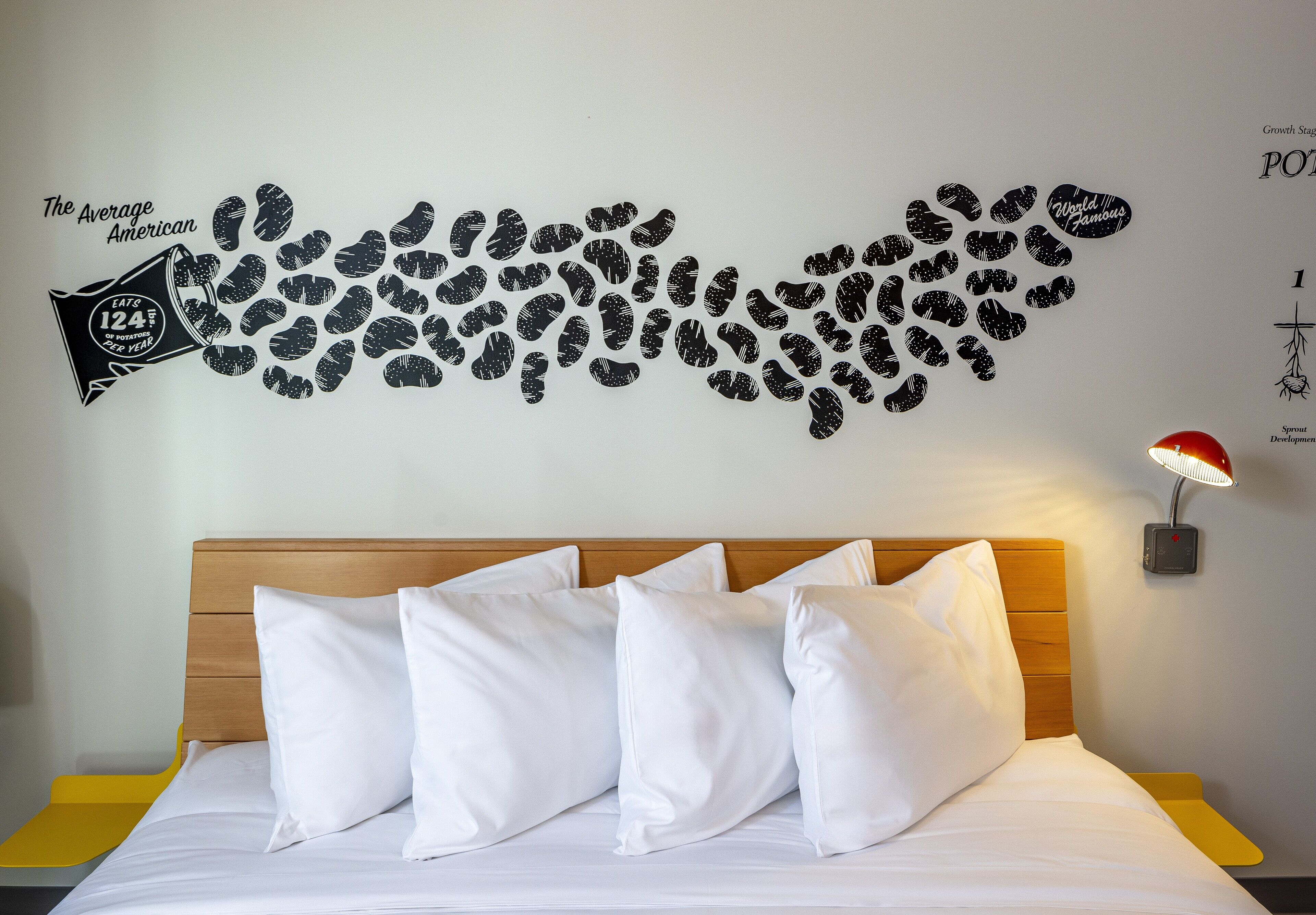A hotel room with a wooden headboard, white bedding, and a wall decal of potato prints.