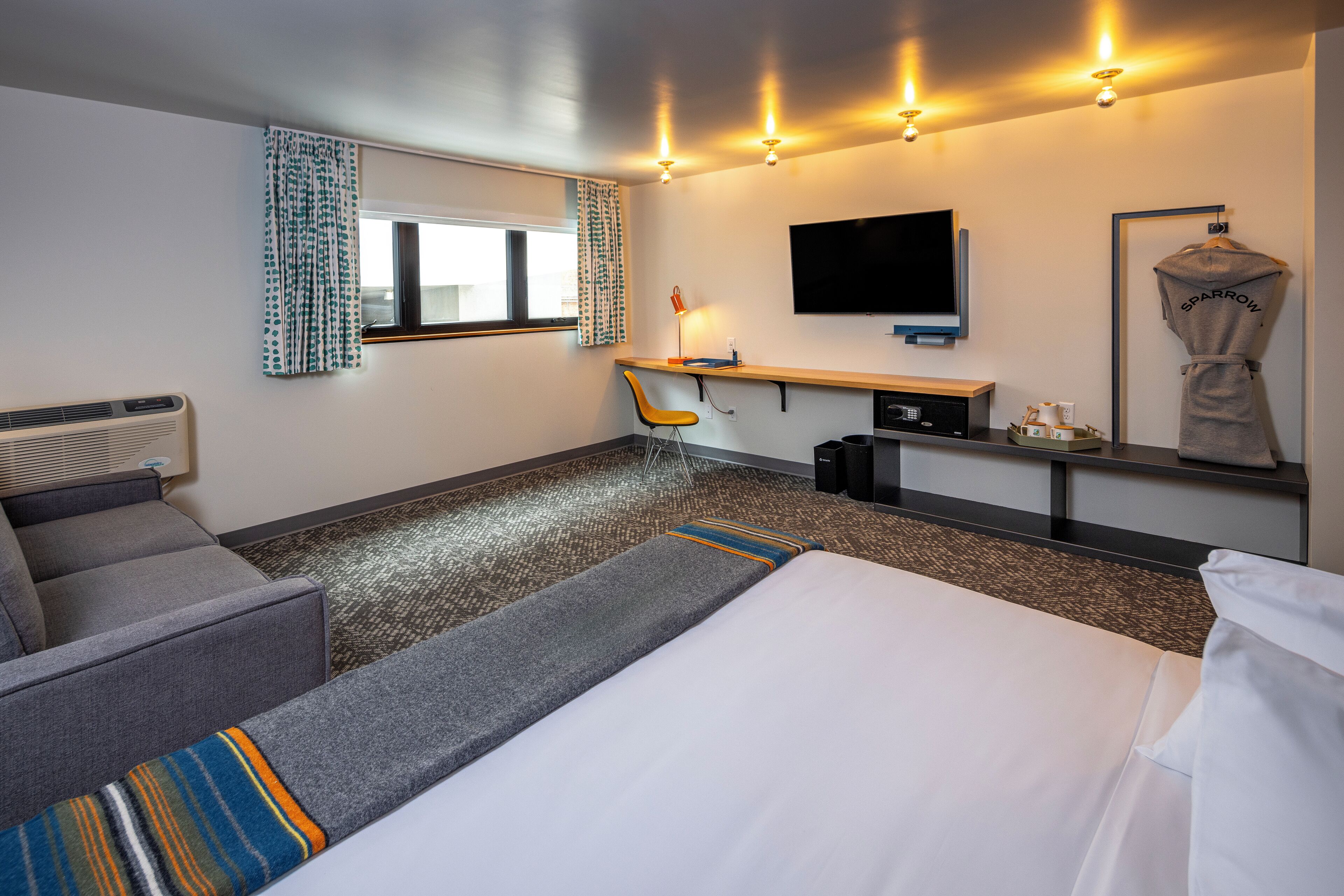 A hotel room with a bed, a desk, a chair, a TV, and a robe hanging on a rack.