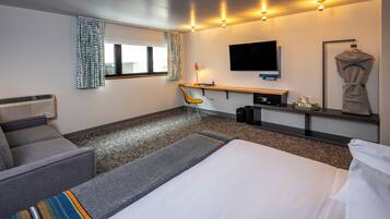 Habitación de hotel con cama, escritorio, silla, televisor y bata colgada en un perchero.